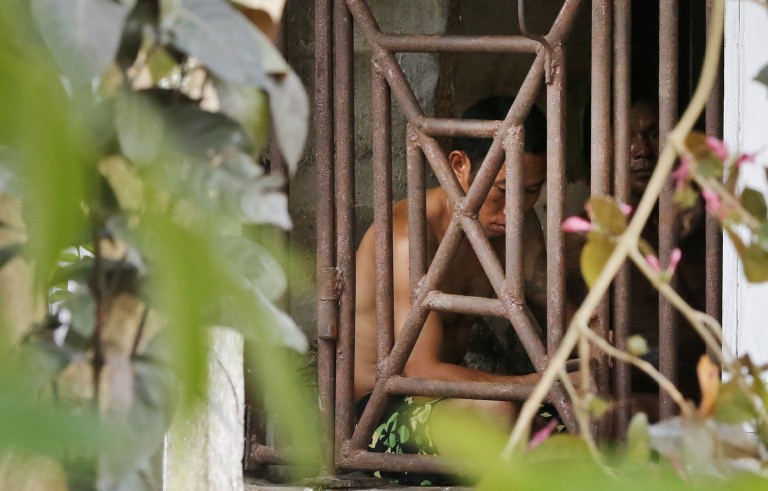 In this Nov. 22, 2014 photo, Thai and Burmese fishing boat workers sit behind bars inside a cell at the compound of a fishing company in Benjina, Indonesia. The imprisoned men were considered slaves who might run away. They said they lived on a few bites of rice and curry a day in a space barely big enough to lie down, stuck until the next trawler forces them back to sea. Photo by Dita Alangkara/Associated Press