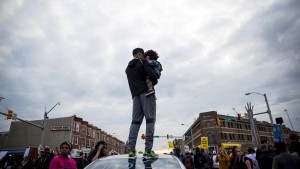 A man holds a child on a car at North Ave and Pennsylvania Ave in Baltimore, Maryland