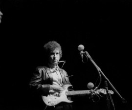 Bob Dylan plays a Fender Stratocaster electric guitar for the first time on stage as he performs at the Newport Folk Festival with guitarist Mike Bloomfield on July 25, 1965 in Newport, Rhode Island. Photo by Alice Ochs/Michael Ochs Archives/Getty Images