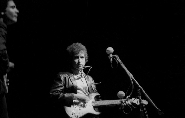 Bob Dylan plays a Fender Stratocaster electric guitar for the first time on stage as he performs at the Newport Folk Festival with guitarist Mike Bloomfield on July 25, 1965 in Newport, Rhode Island. Photo by Alice Ochs/Michael Ochs Archives/Getty Images