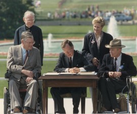 George Bush signs the Americans with Disabilities Act of 1990; standing left  to right Reverend Harold Wilkie, Sandra Parrino of the National Council on Disability; seated left to right, Evan Kemp, Chairman of the Equal Employment and Opportunity Commission, George Bush, Justin Dart, Chairman of the 's Committee on the Employment of People with Disabilities. Washington DC, USA, 26 July 1990. (Photo by Fotosearch/Getty Images).
