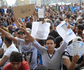 Refugees raise their documents and railways tickets outside the Keleti station in Budapest, Hungary September 2, 2015. Hundreds of migrants protest in front of Budapest's Keleti Railway Terminus for a second straight day on Wednesday, shouting "Freedom, freedom!" and demanding to be let onto trains bound for Germany from a station that has been closed to them by Hungarian riot police officers. REUTERS/Bernadett Szabo - RTX1QSEO