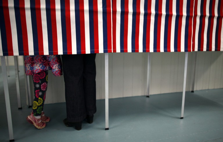 A girl tiptoes to see a woman's ballot while voting in the primary election at Deerfield Town Hall in Deerfield