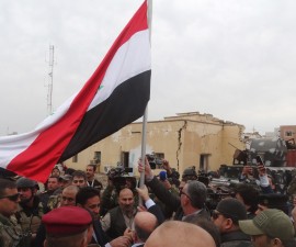 Iraqi Prime Minister Haider al-Abadi (C, back to camera) holds an Iraqi flag in the city of Ramadi, December 29, 2015. Abadi on Tuesday visited Ramadi a day after the army retook the city centre from Islamic State, a victory that could help vindicate his strategy for rebuilding the military after stunning defeats in the past 18 months. REUTERS/Stringer EDITORIAL USE ONLY. NO RESALES. NO ARCHIVE - RTX20FCL