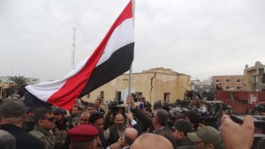 Iraqi Prime Minister Haider al-Abadi (C, back to camera) holds an Iraqi flag in the city of Ramadi, December 29, 2015. Abadi on Tuesday visited Ramadi a day after the army retook the city centre from Islamic State, a victory that could help vindicate his strategy for rebuilding the military after stunning defeats in the past 18 months. REUTERS/Stringer  EDITORIAL USE ONLY. NO RESALES. NO ARCHIVE - RTX20FCL