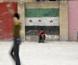 Boys play at a school's playground as one of them sits in front of a wall painted with an opposition flag in the rebel-controlled area of Aleppo's Seif al-Dawla, Syria October 25, 2015. REUTERS/Hosam Katan      EDITORIAL USE ONLY. NO RESALES. NO ARCHIVE - RTX1T67Z