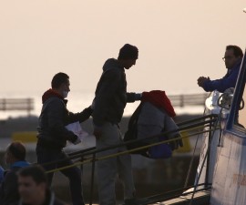 A Frontex officer (L) escorts a migrant as he boards on a Turkish-flagged passenger boat to be returned to Turkey, on the Greek island of Lesbos, April 4, 2016. REUTERS/Giorgos Moutafis - RTSDFLL