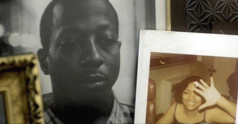Two photos leaning against a wall. The leftmost photo is a black and white portrait of a Black man in his late teens/early twenties looking down. This photo is in a wood and gold frame. Next to it is a photo of an Black woman in her twenties. She is smiling and covering the camera with one hand. The photo seems to be a poloroid.