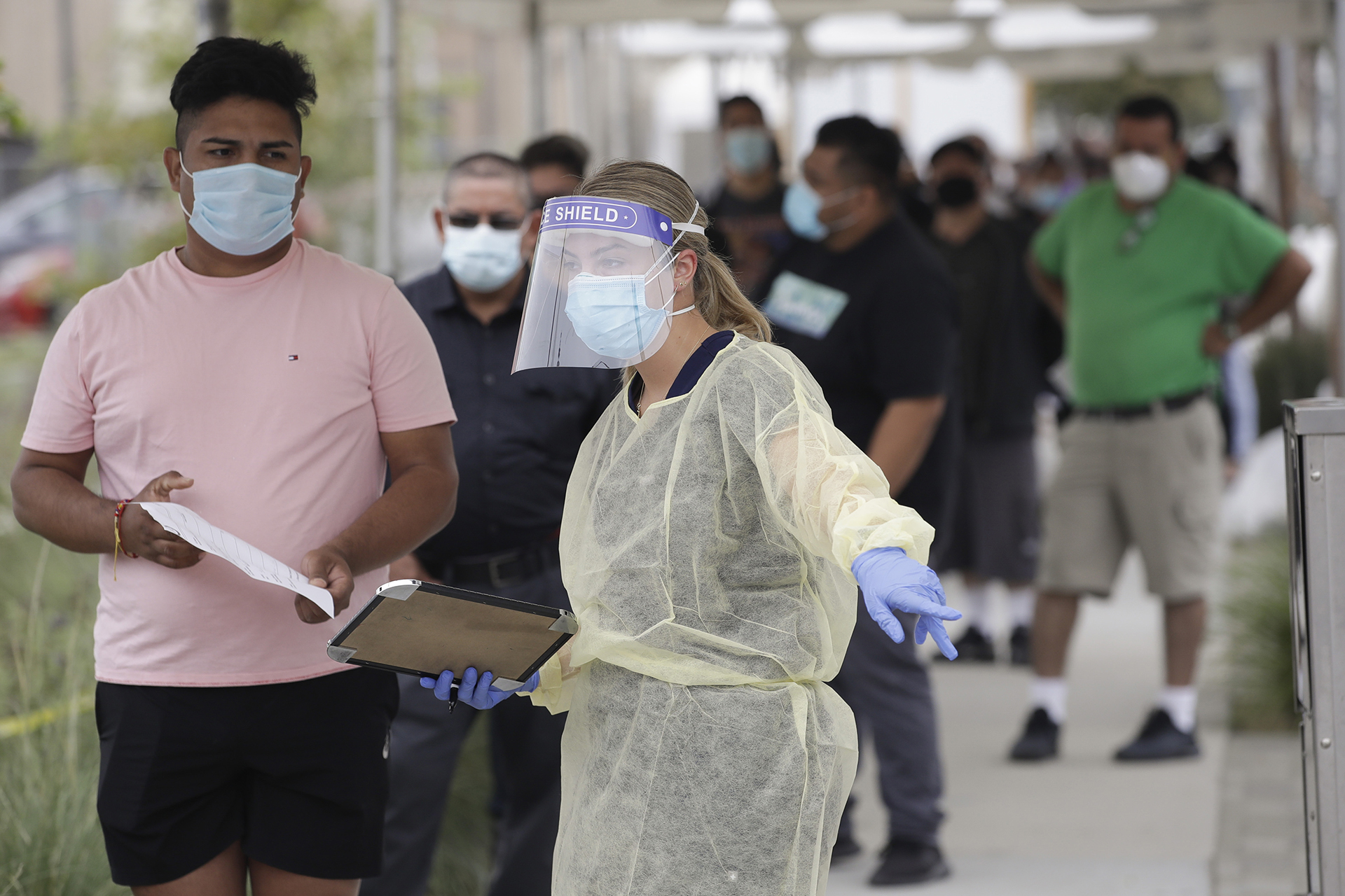 FILE - In this July 22, 2020, file photo, people line up behind a health care worker at a mobile coronavirus testing site at the Charles Drew University of Medicine and Science in Los Angeles. Although it will take years for researchers to understand why the pandemic was disproportionately worse in the U.S., early studies that compare different countries’ responses are finding that U.S. shortages of masks, gloves, gowns, shields, testing kits and other medical supplies indeed cost lives.