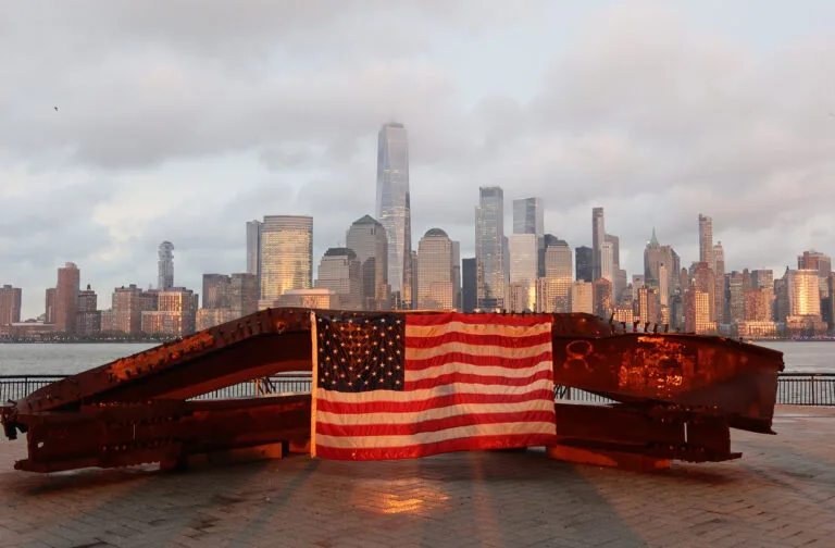 The sun sets on a flag at a 9/11 memorial in Jersey City, New Jersey, with the skyline of lower Manhattan in the background, on April 15, 2021.
