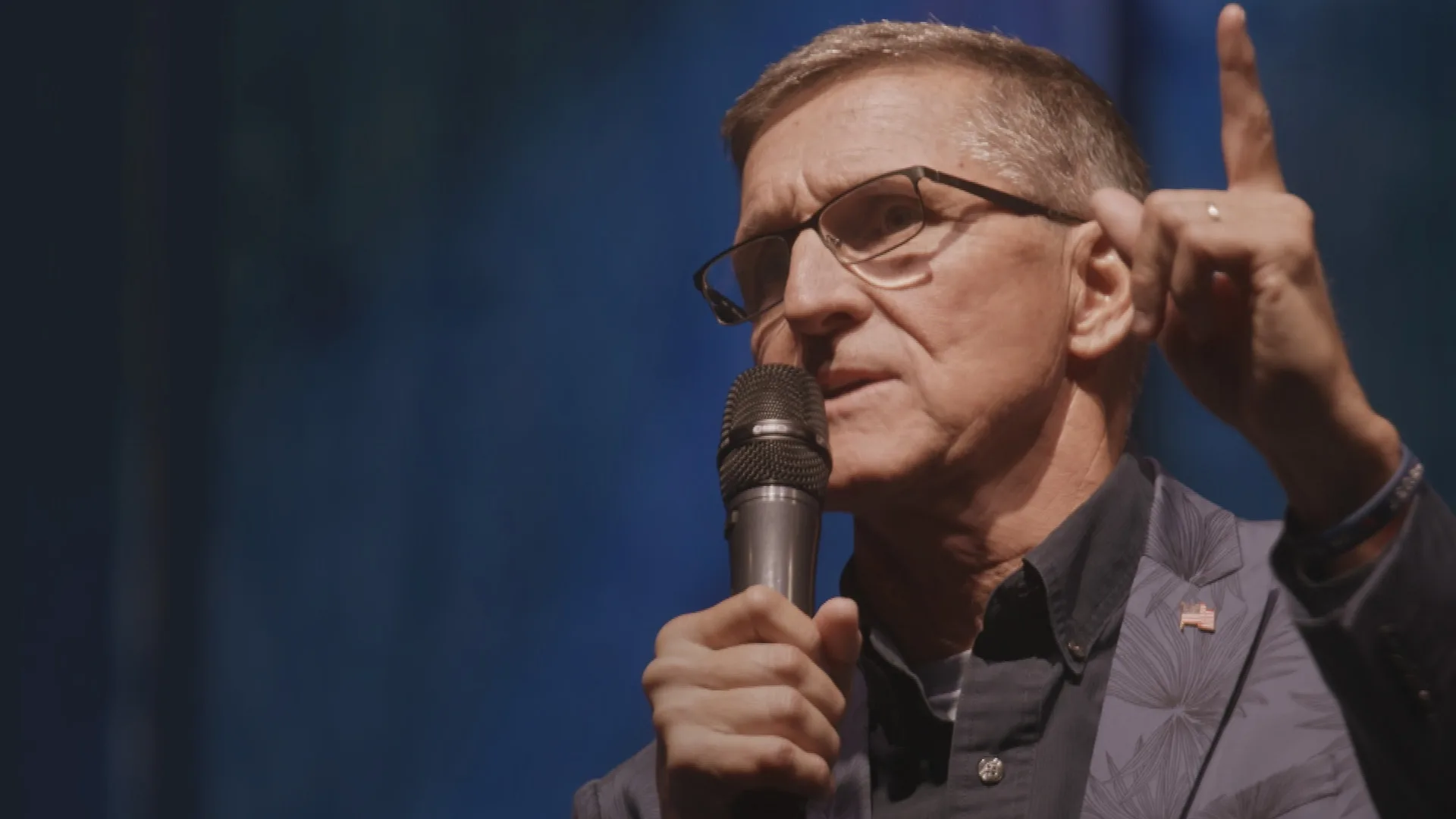 An image of retired three-star general Michael Flynn holding a microphone and raising a finger.