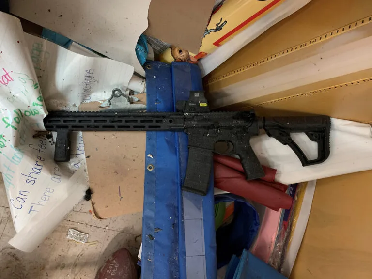 An AR-15 lies in a pile of debris.