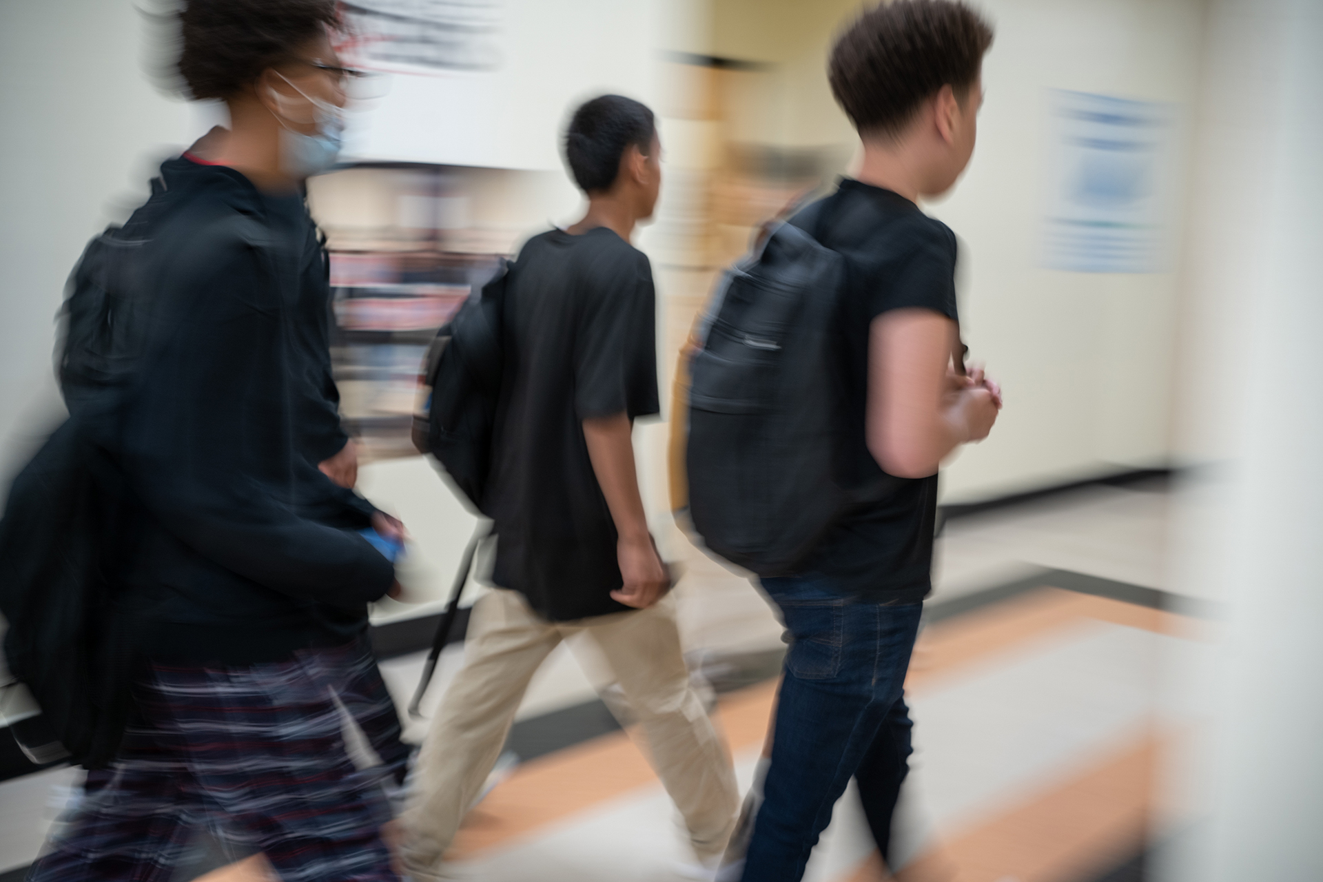 Three high school kids walk down a hallway carrying backpacks.
