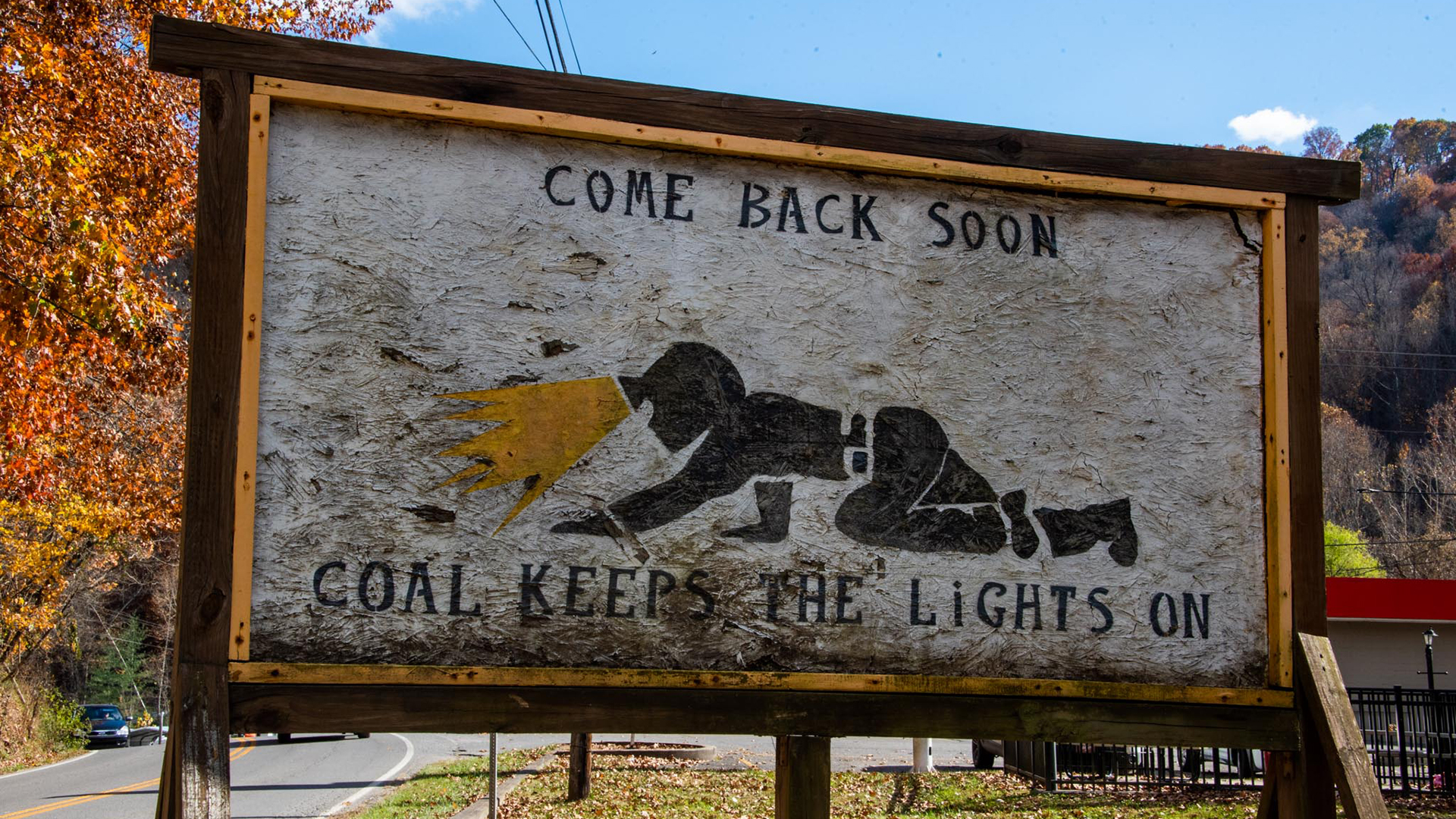 A makeshift billboard with an illustration of a miner and text that reads come back soon and coal keeps the lights on.