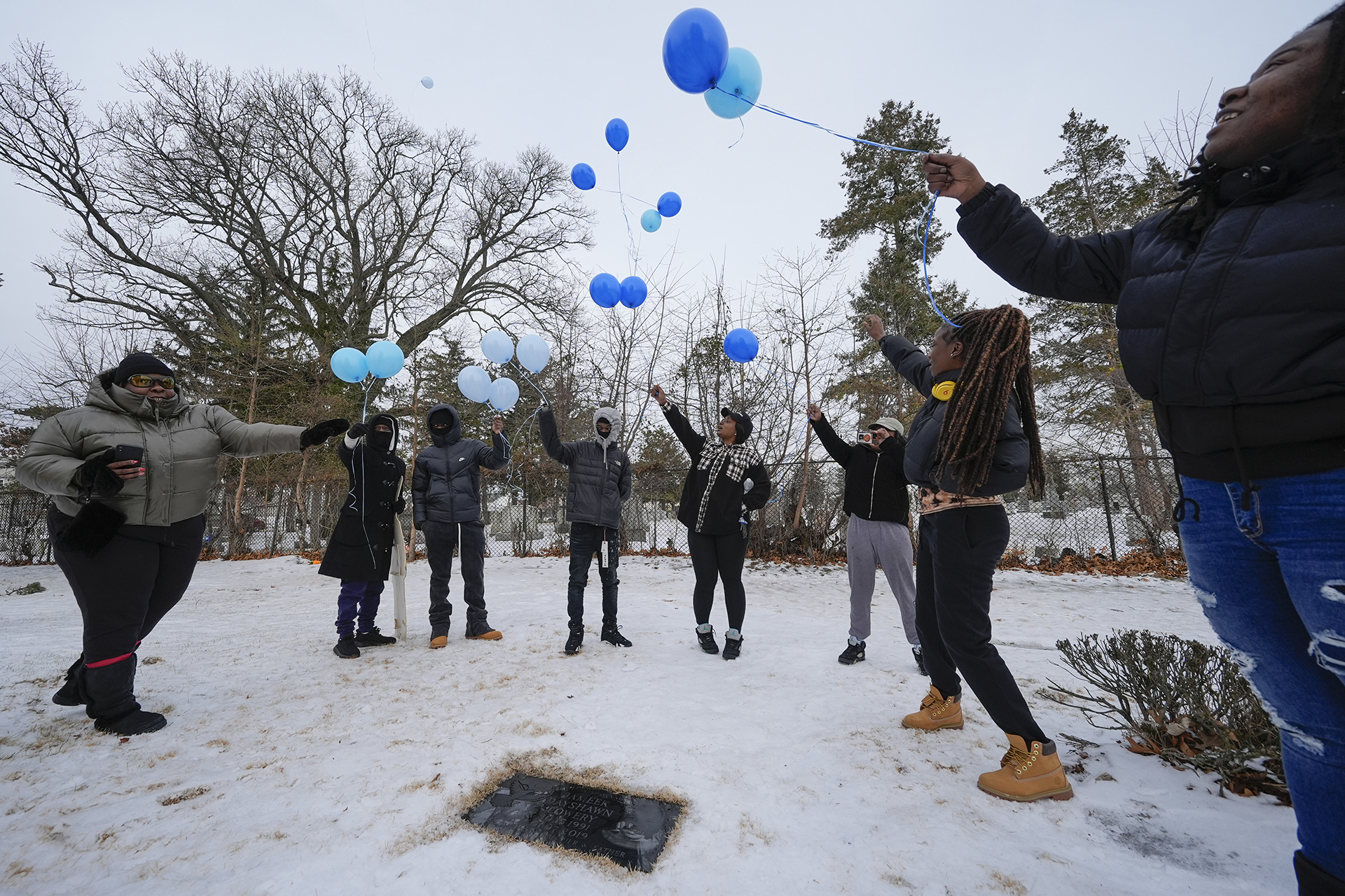 Several people stand on snow-covered ground holding balloons of different shades of blue.