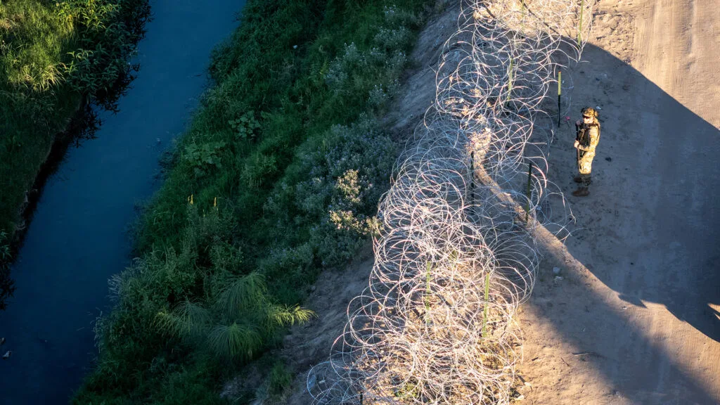 A Texas National Guard soldier stands behind a barbed wire fence.
