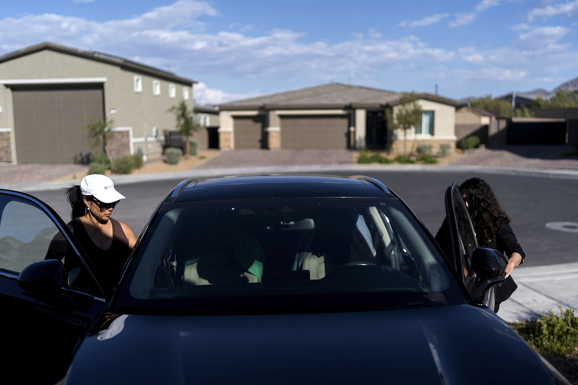 Two women get into a car parked in a driveway.
