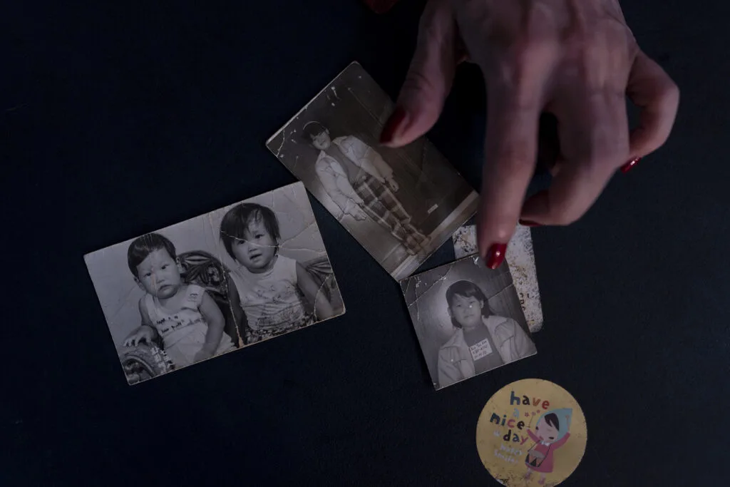 Yooree Kim's hands on several black and white childhood photos of her and her brother and a sticker that reads have a nice day with an illustration of a young girl beating a drum.