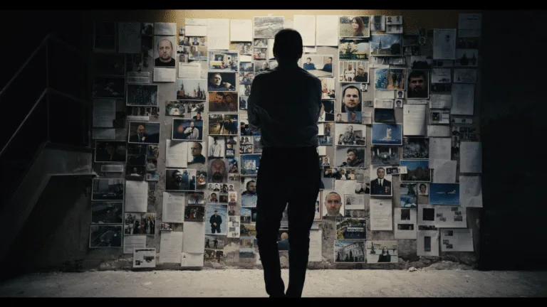 A man's silhouette in front of a wall covered with photos and papers.