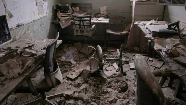 An office room with the ground, tables and chairs broken and covered in debris from Hurricane Helene.
