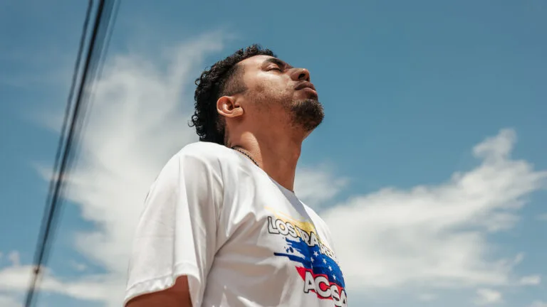 A man stands in the sunlight with his eyes closed and his head tilted up. Above him is the open sky.