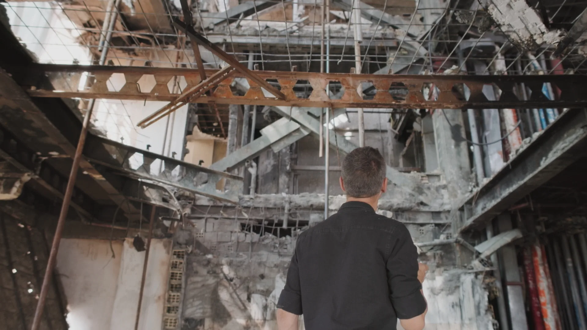 A man looks up inside a destroyed building with exposed metal rods and girders and shattered concrete.