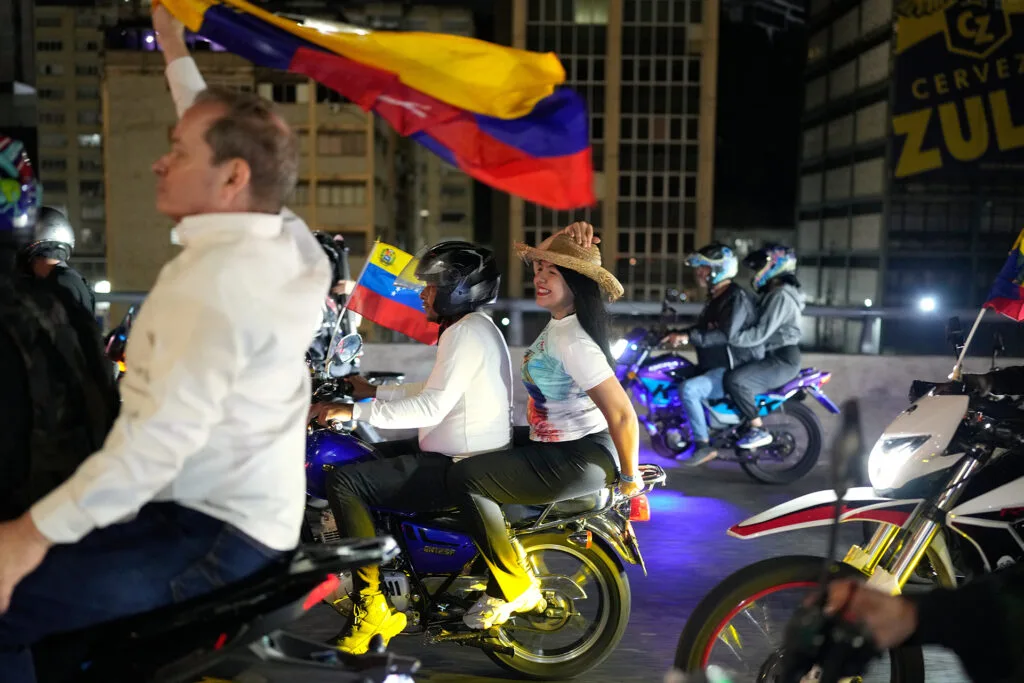 People ride motorbikes at night, some holding Venezuelan flags.