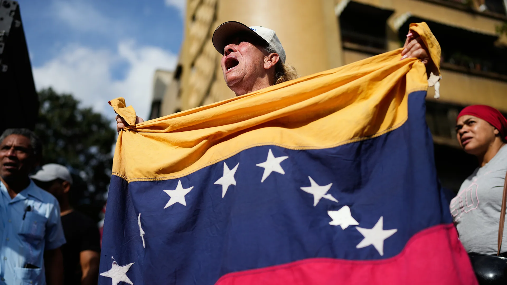 A person wearing a hat holds a Venezuelan flag and shouts.