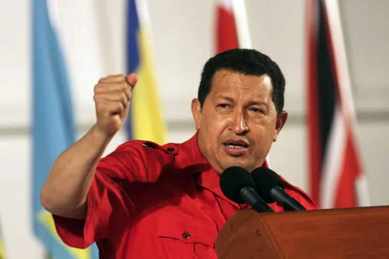 Venezuelan President Hugo Chávez gestures while speaking at a podium before a row of flags.