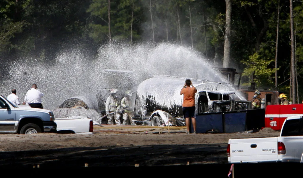 Several firefighters spray foam on a tanker truck that caught fire.