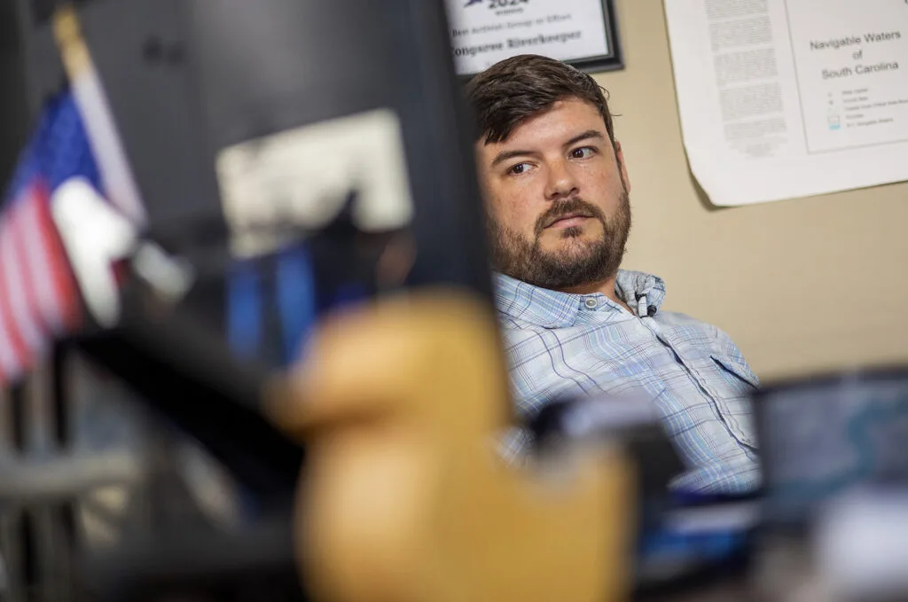 Bill Stangler is seated behind a computer screen and an American flag.