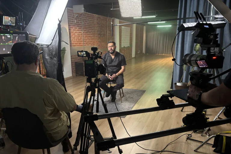 Óscar Martínez being interviewed by a man viewed from the back in a room with several cameras and monitors in the foreground.