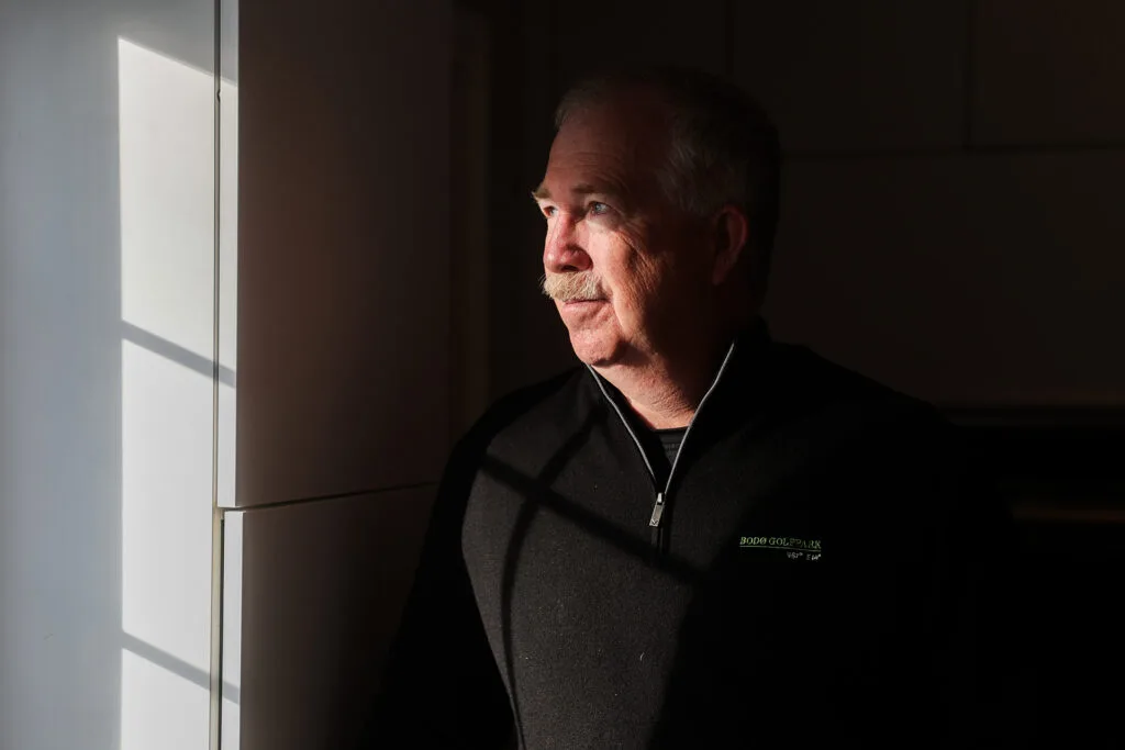 A man standing in shadow looking out of a sunny window.