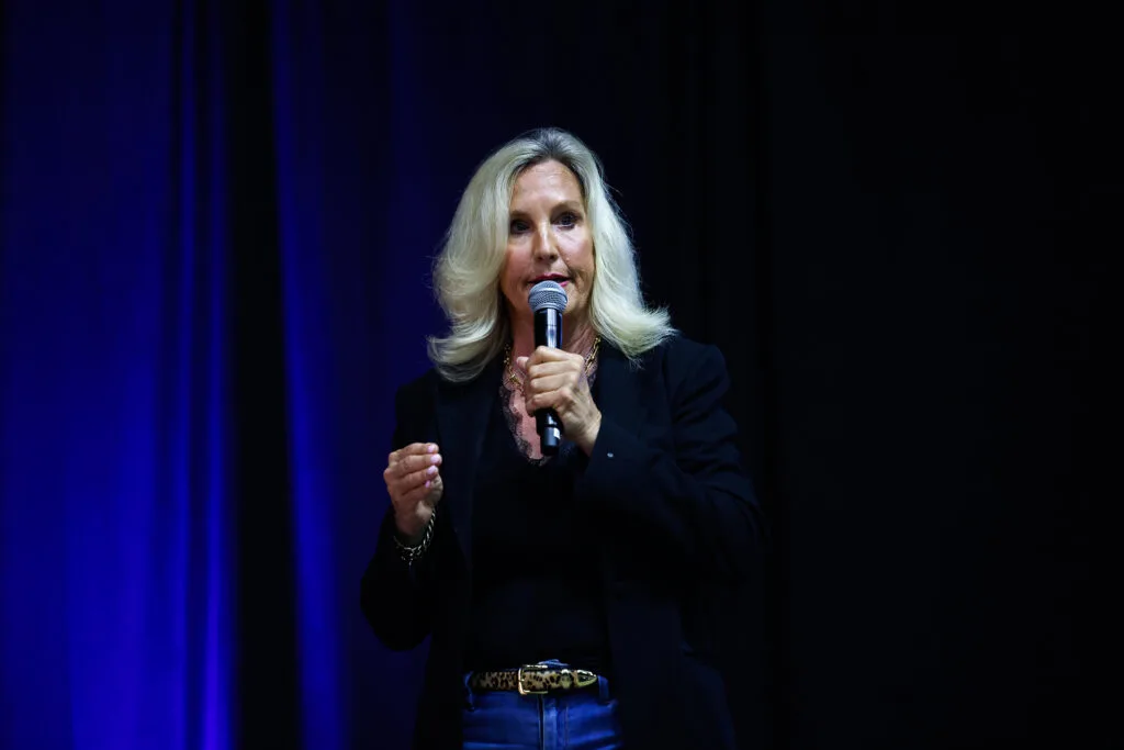 A woman holding a microphone and standing on a stage in front of a blue curtain.