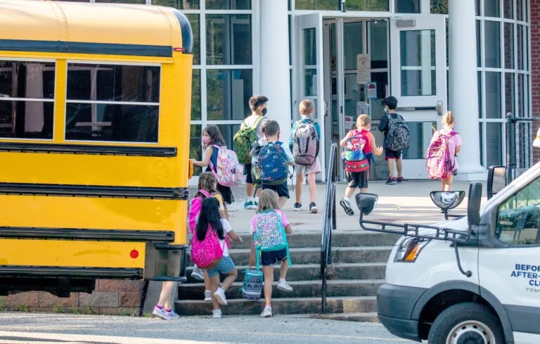 Young students wearing masks walk up stairs to enter the building of Bethel Memorial Elementary School.