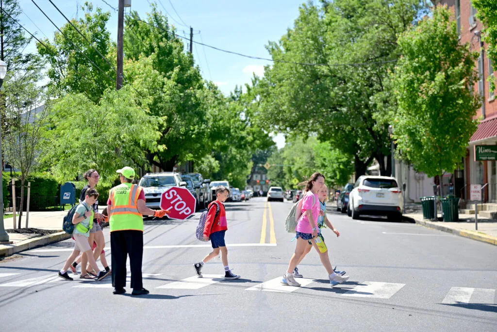 A crossing guard holds a stop sign as several children wearing backpacks walk across a street.