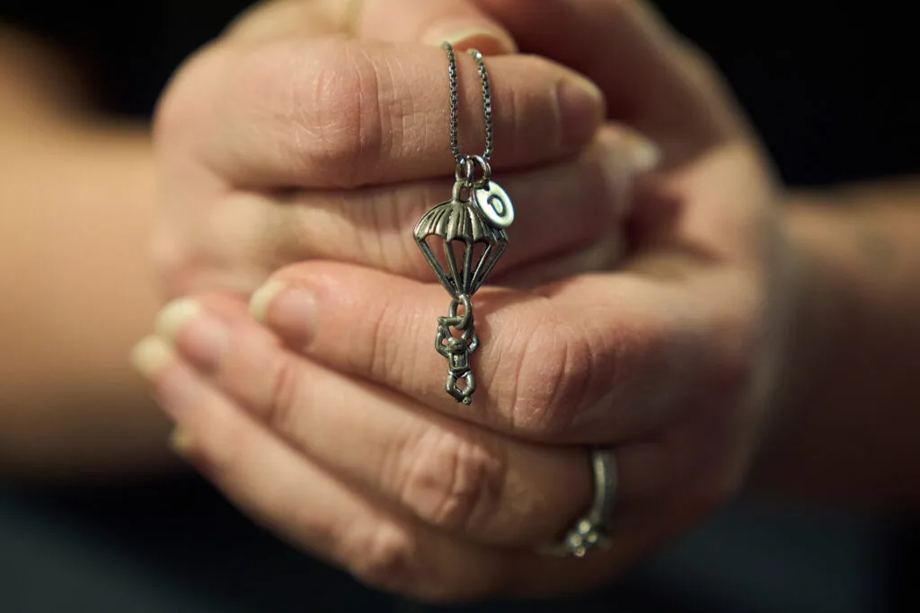 Close up of two hands holding a necklace with a charm hanging from it that shows a figure hanging from a parachute.