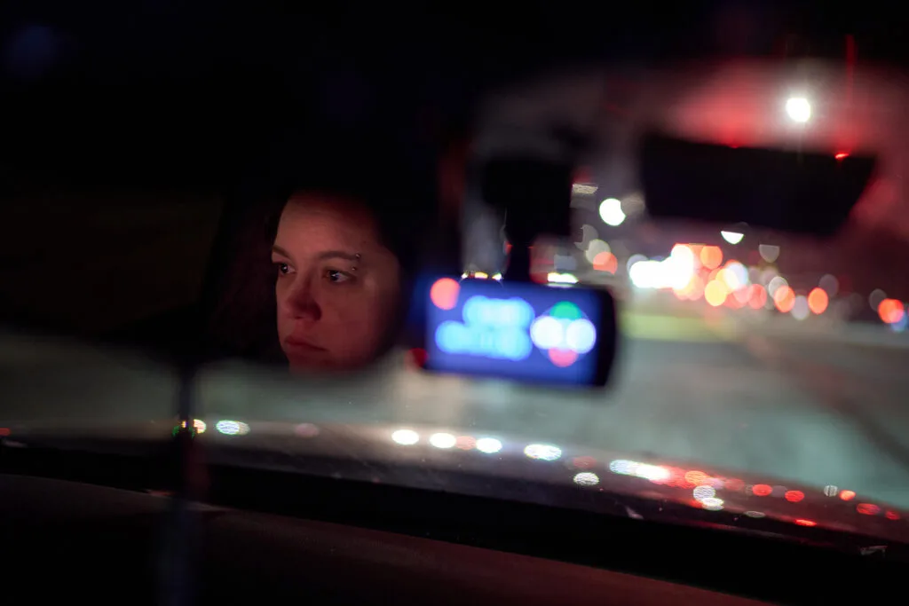 A woman's face is reflected in a rearview mirror of a car at night.