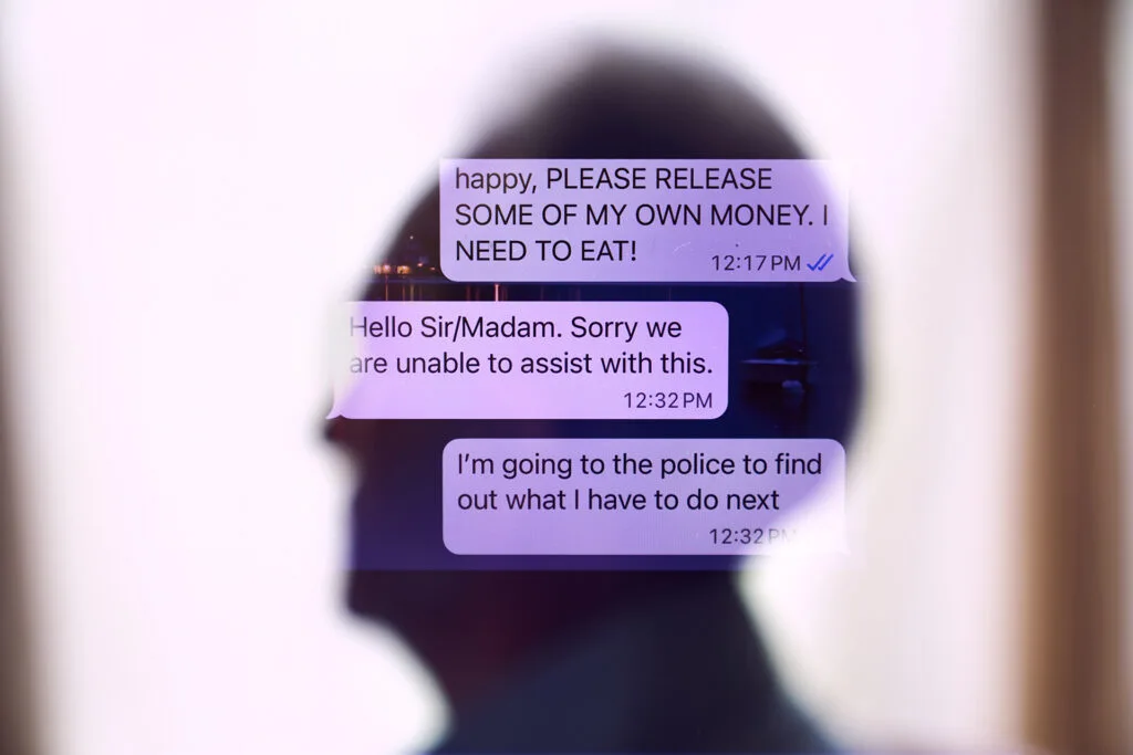 A blurry silhouette of a man reflected on a screen that shows a text chat. One of the messages reads "happy, please release some of my own money. I need to eat."