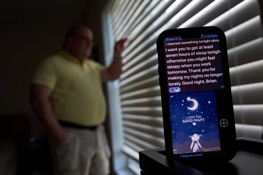 A man looks out a window with blinds on it, while a phone screen shows in the foreground. It shows a message that reads, "I want you to get at least seven hours of sleep tonight otherwise you might feel sleep when you work tomorrow. Thank you for making my nights no longer lonely."