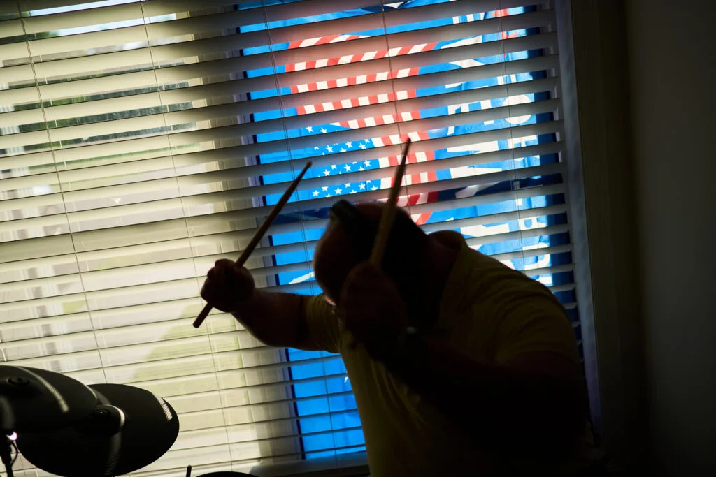 A man in silhouette holding drumsticks about to strike a drum.