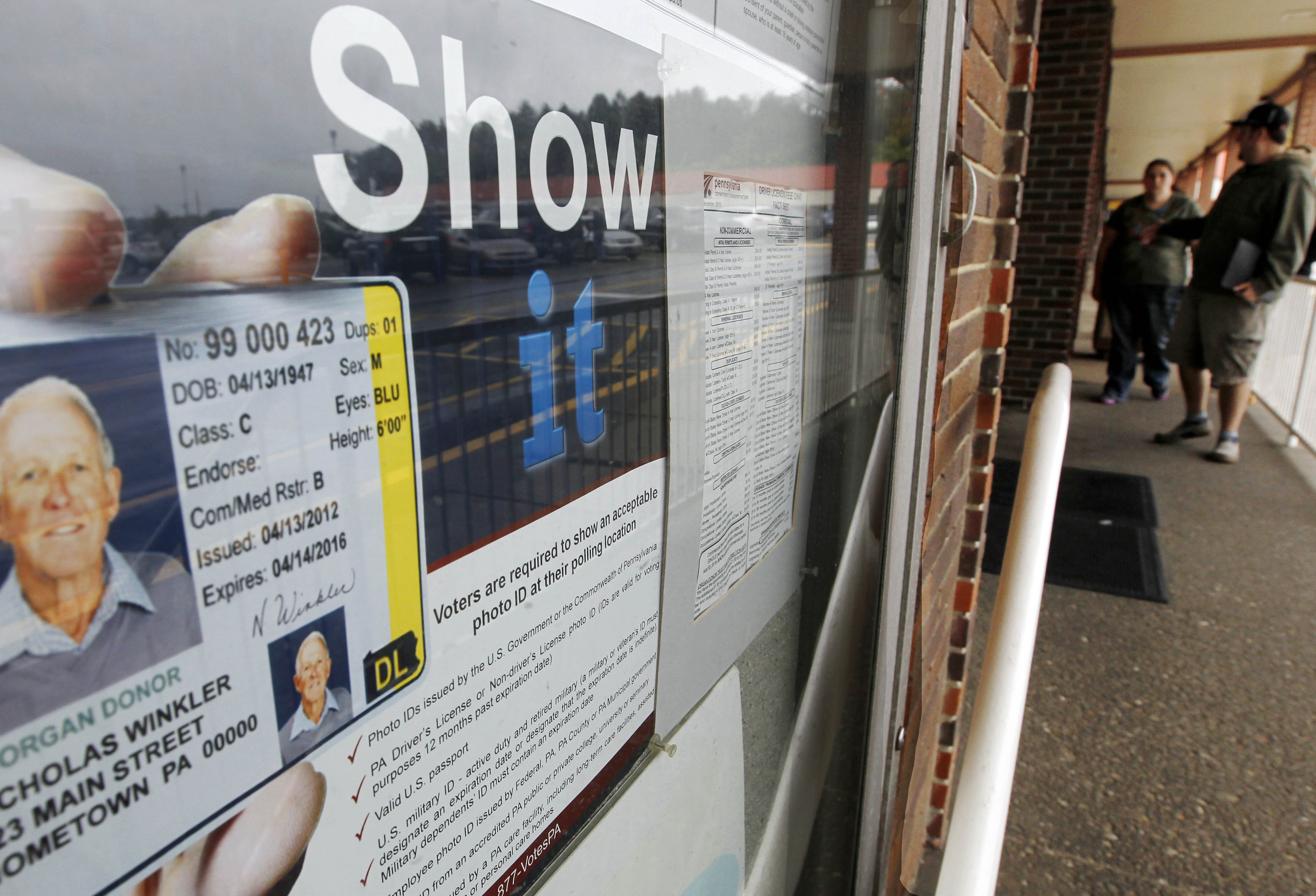In this Sept. 26, 2012 file photo People pass the signs telling of the requirement for voters to show an acceptable photo ID to vote as they head into the the Penndot Drivers License Center in Butler, Pa.