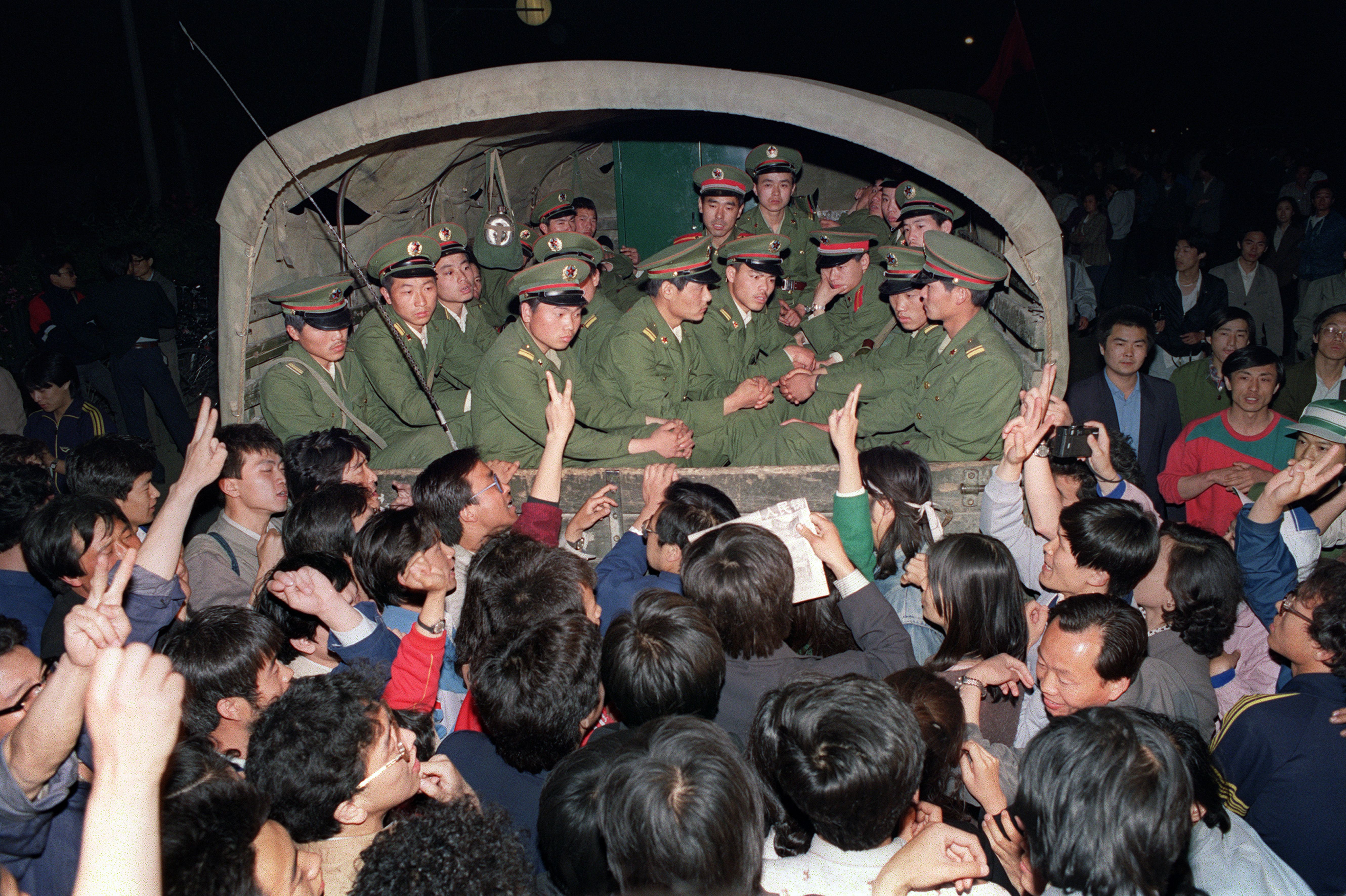 Pro-democracy demonstrators raise their fists and flash Victory signs 20 May 1989 in Beijing as they stop the military truck filled with soldiers on its way to Tiananmen Square 20 May 1989.