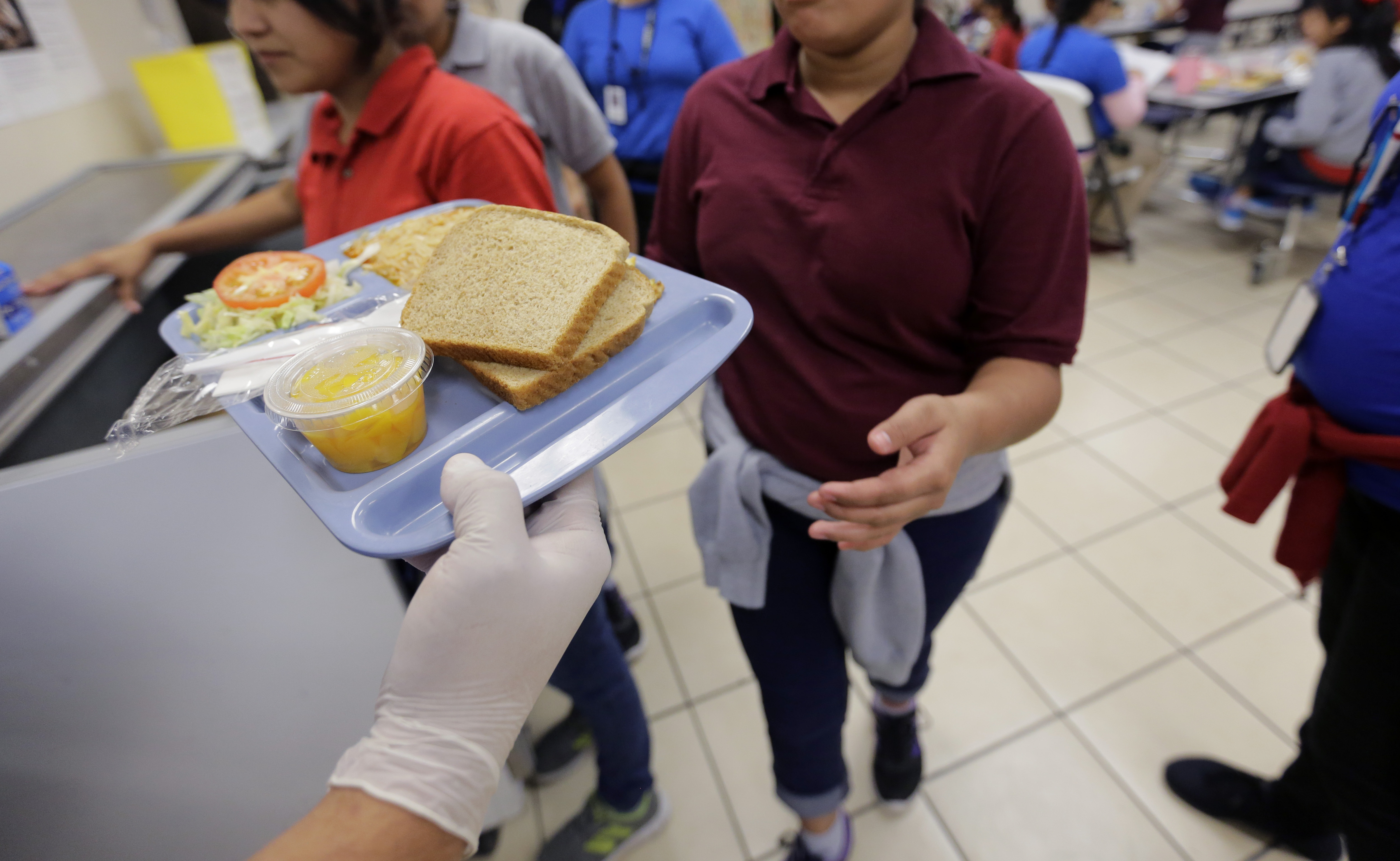A teen reaches out to take a tray of cafeteria food.