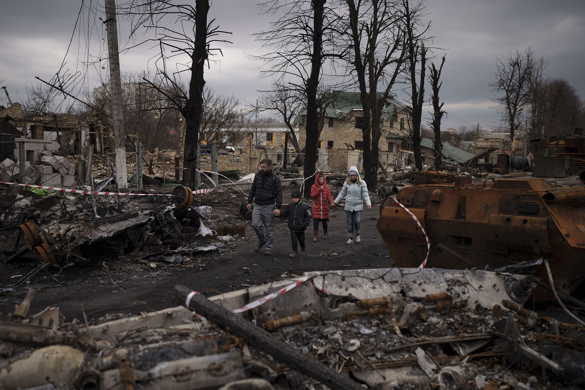 FILE - A family walks amid destroyed Russian tanks in Bucha, on the outskirts of Kyiv, Ukraine, Wednesday, April 6, 2022.