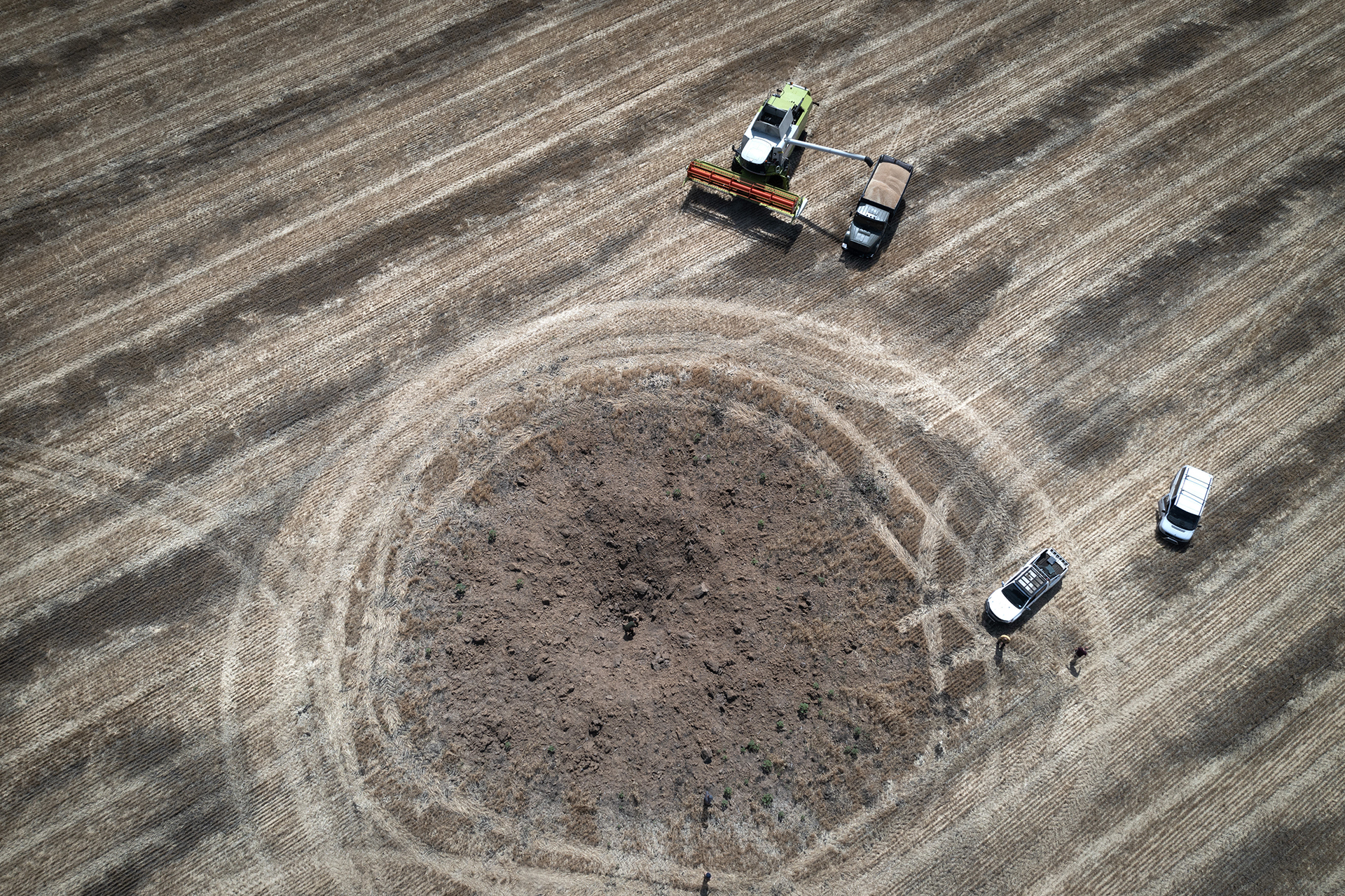 FILE - Next to a crater left by a Russian rocket, a farmer harvests a field 10 kilometers (6 miles) from the front line between Russian and Ukranian forces, in the Dnipropetrovsk region, Ukraine, Monday, July 4, 2022. (AP Photo/Efrem Lukatsky, File)