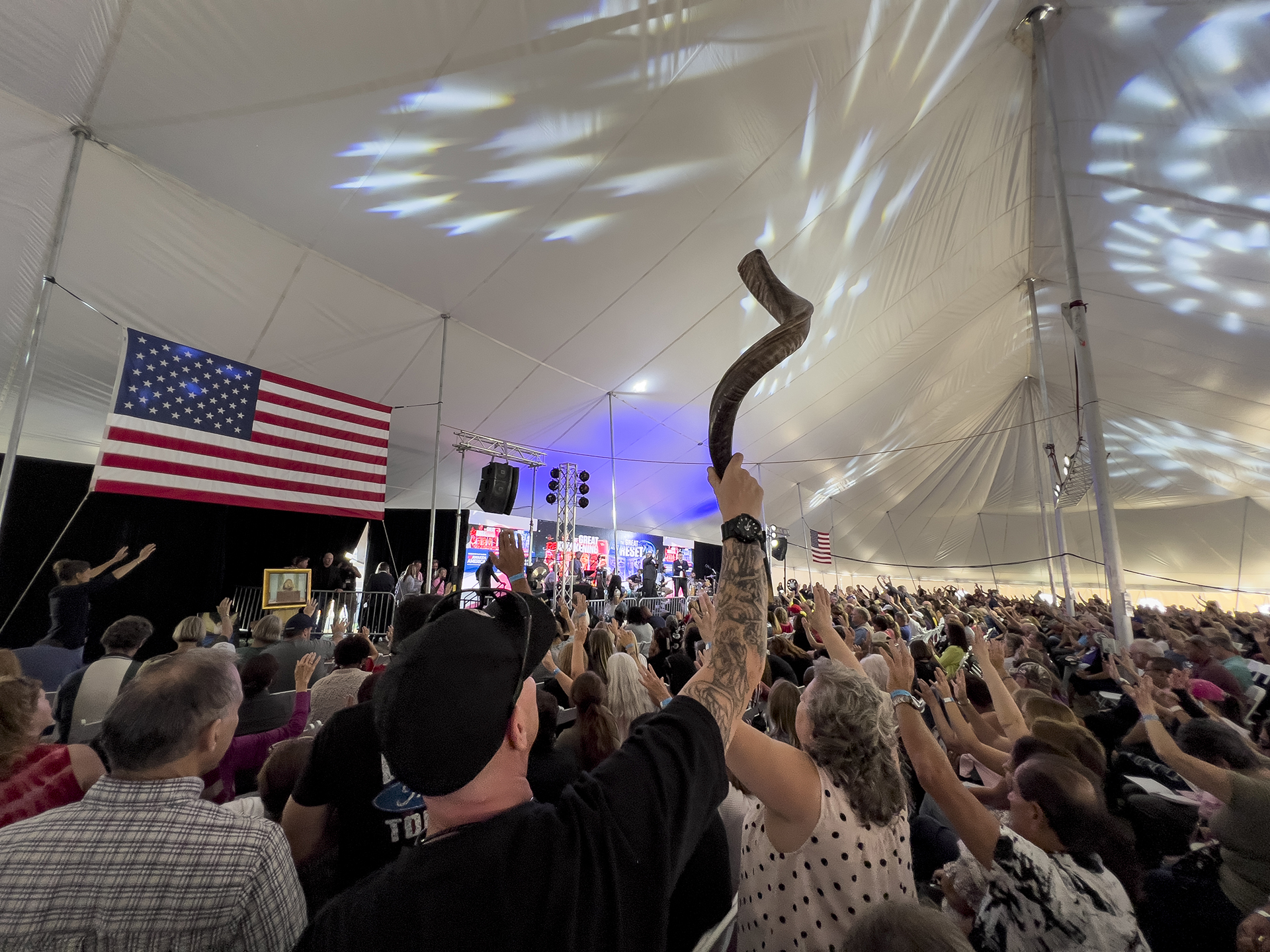 A man holds high a shofar as the crowd prays inside the tent during the ReAwaken America tour at Cornerstone Church in Batavia, N.Y., Friday, Aug. 12, 2022. The instrument used in some Jewish worship services has been adopted by the far right, and several people blew shofars to open the conference. (AP Photo/Carolyn Kaster)