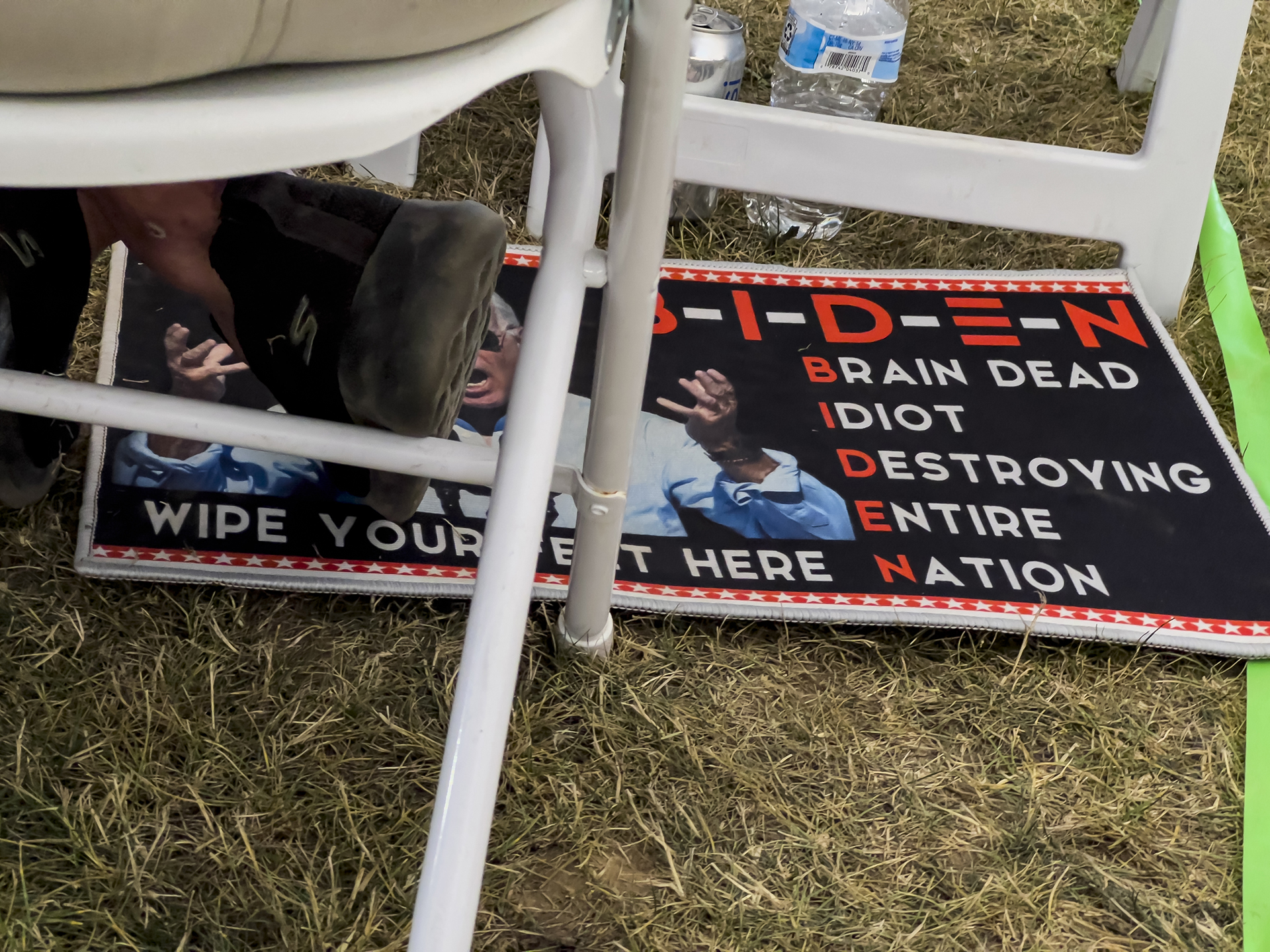 A man sits with his feet on a doormat critical of President Joe Biden during the ReAwaken America tour at Cornerstone Church in Batavia, N.Y., Saturday, Aug. 13, 2022. (AP Photo/Carolyn Kaster)