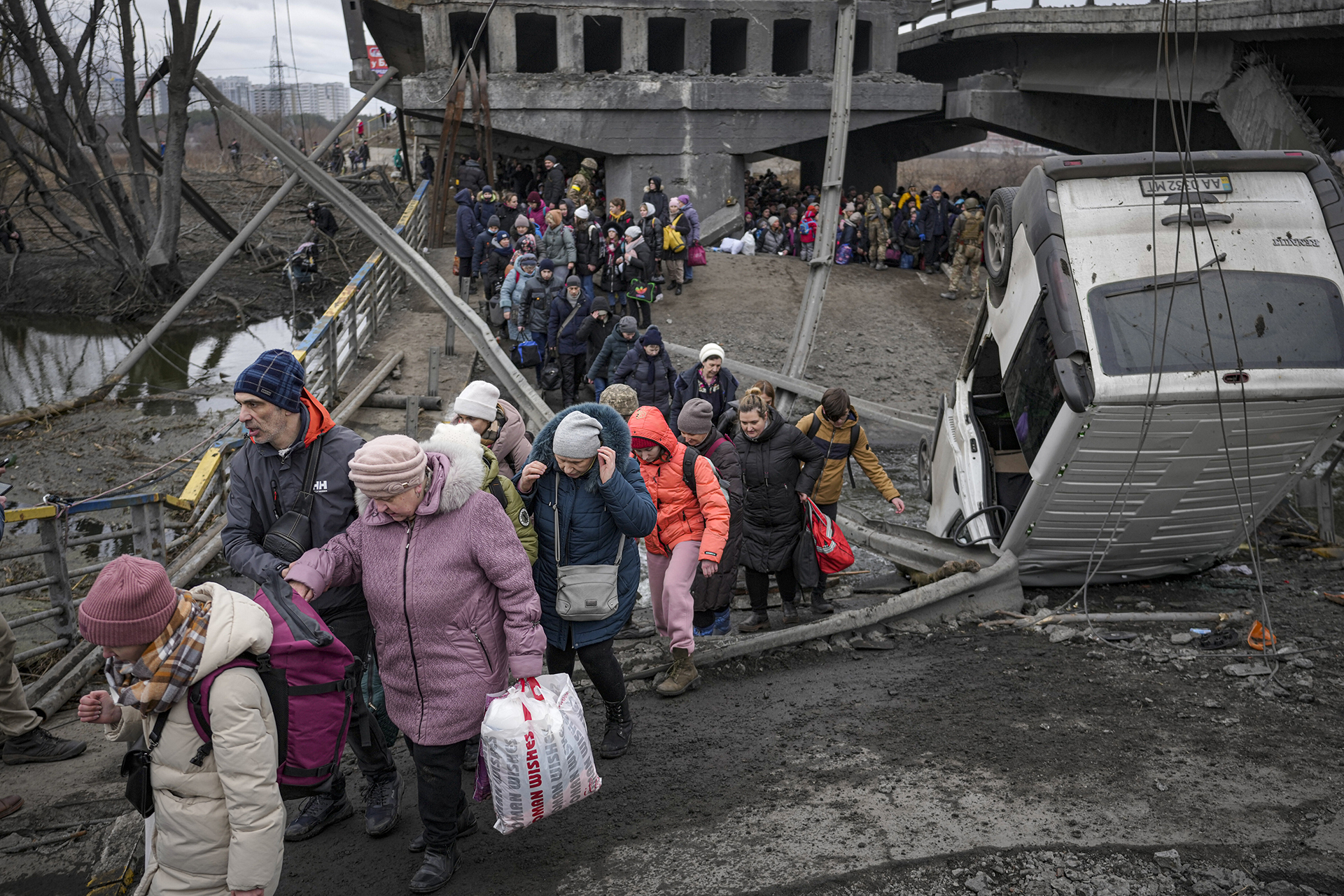 People walk along an improvised path under a bridge that was destroyed by Ukrainian troops designed to slow any Russian military advances, as they flee Irpin, Ukraine, Saturday, March 5, 2022. (AP Photo/Vadim Ghirda, File)