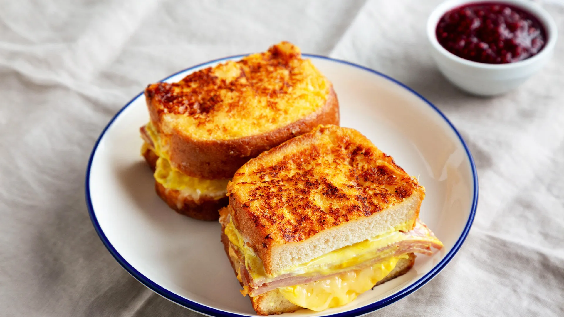 Color photo of a batter-fried Monte Cristo sandwich on a plate with a side of jam.